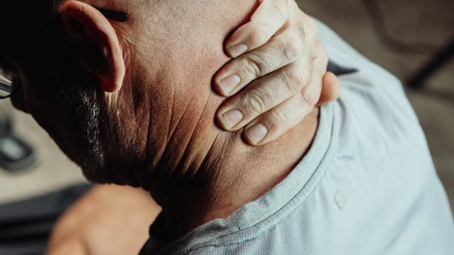 Man with neck pain holding head, indicating neck and shoulder injury.